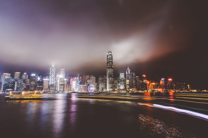 City lights across a harbour at night with light trails on the water.