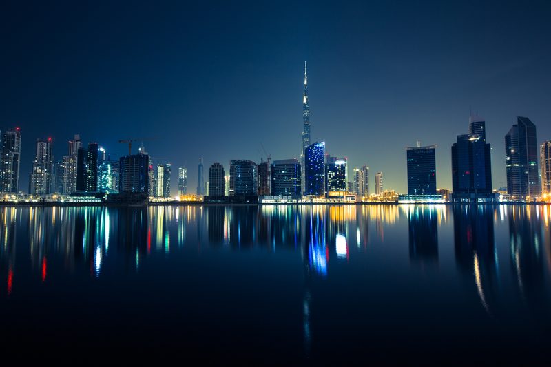 A modern city skyline at night reflected across still water.